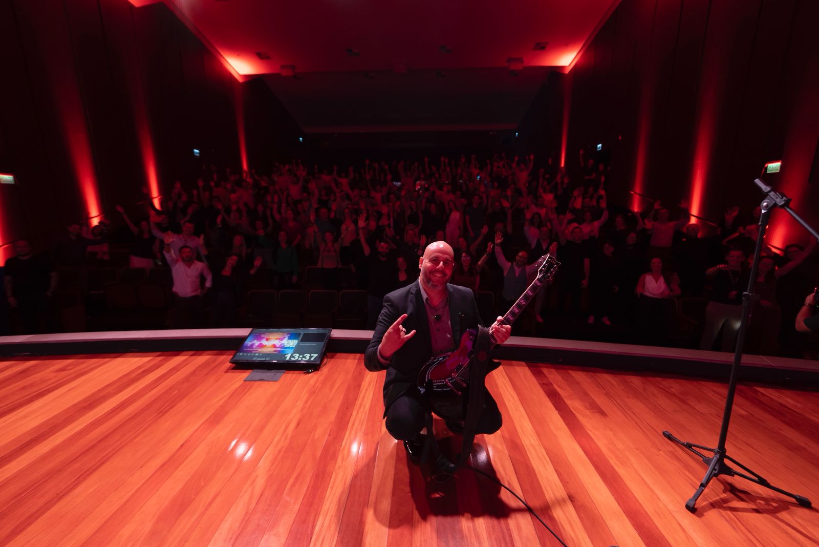 Rodrigo Simões em palco com plateia em pé ao fundo